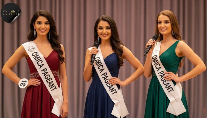 Three Indian beauty pageant contestants wearing OMICA PAGEANT sashes on stage with a soft Omica Pageant logo in the background.
